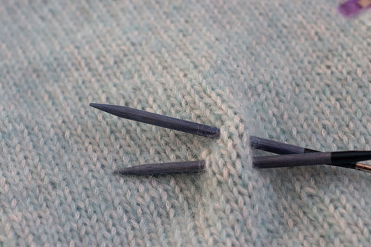 Two knitting needles with yarn on a knitted surface